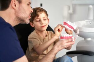 Dentist teaching a child about proper oral care using a dental model during a dental checkup