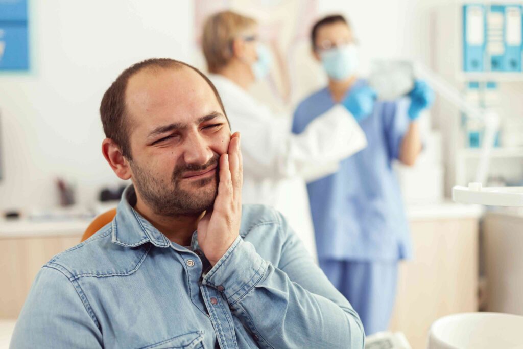 Man holding his cheek in pain while waiting at a dental office.