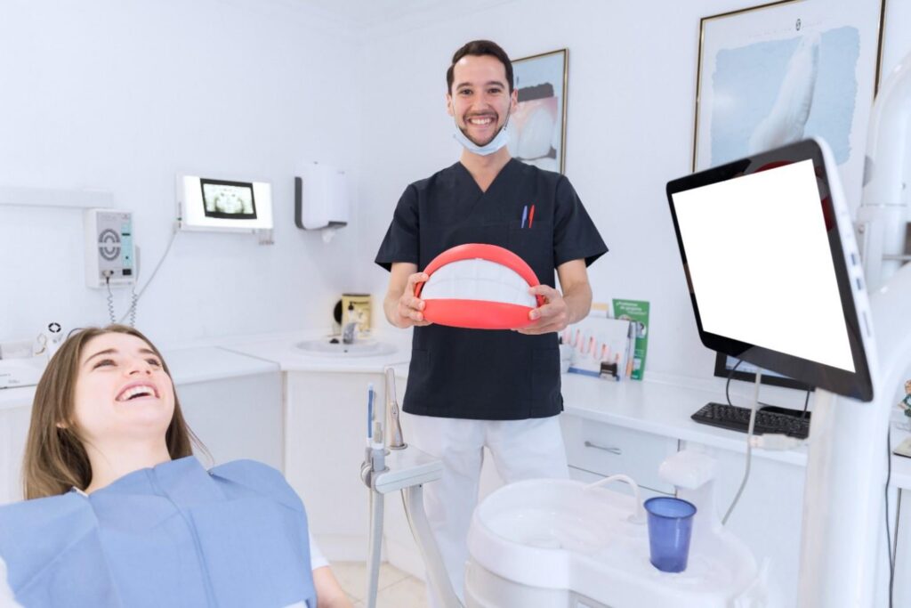 Dentist showing oversized tooth model to smiling patient.