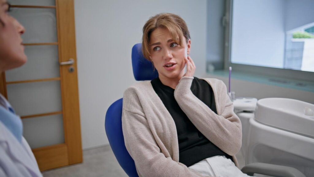 Patient holding jaw while discussing tooth pain with dentist.