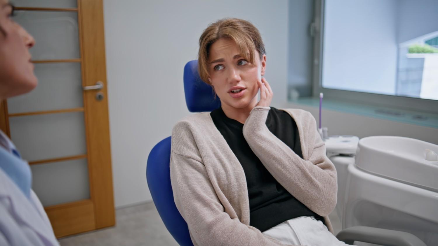 Patient holding jaw while discussing tooth pain with dentist.