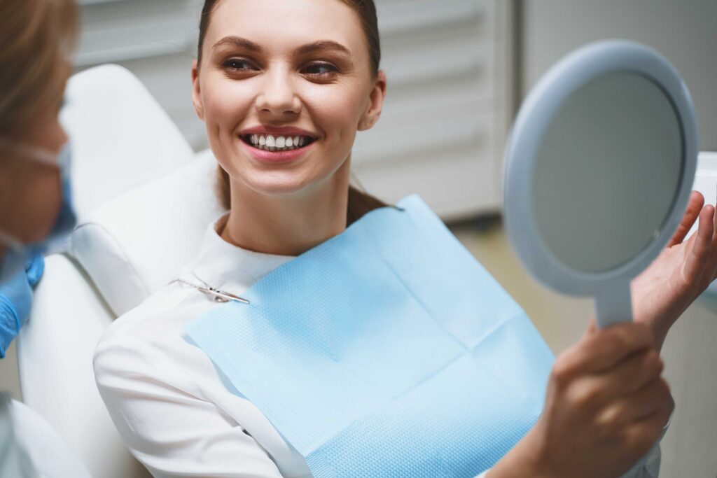 Patient smiling while holding a mirror after dental visit