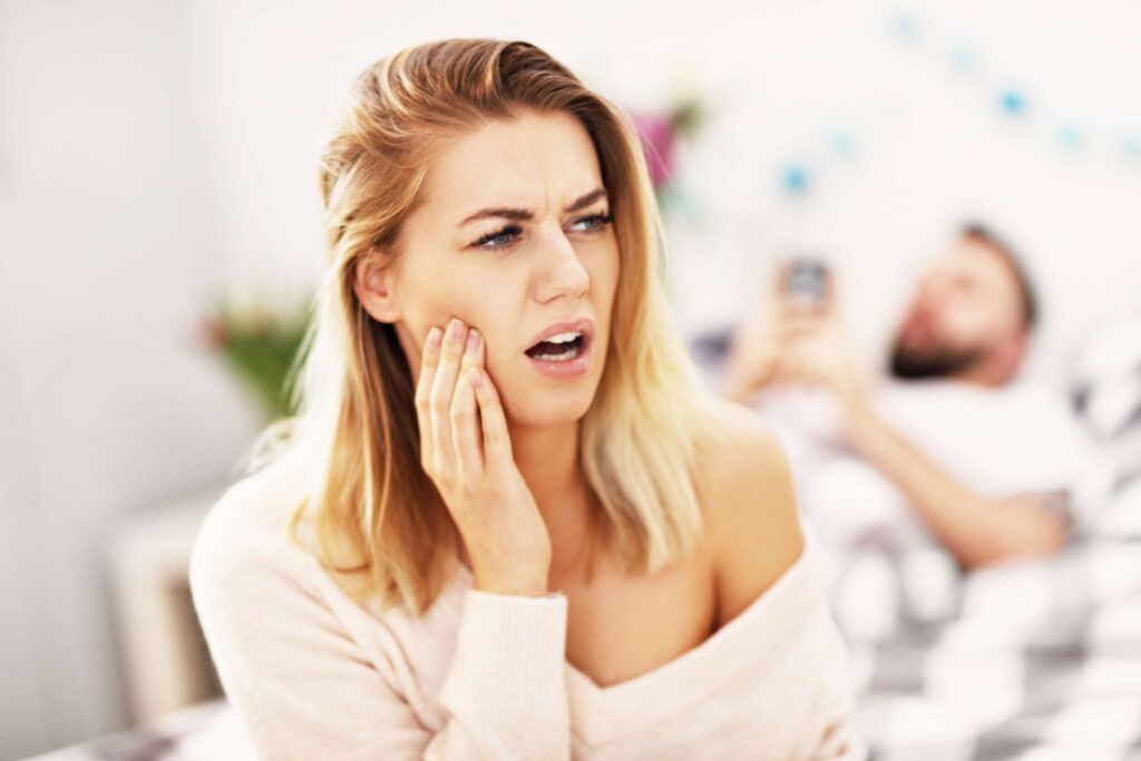 Woman holding her jaw from tooth pain at home
